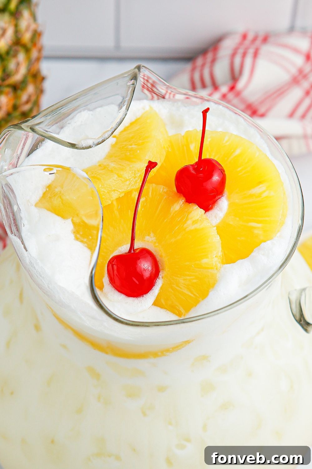 Island Escape Punch 9 Close-up of the Piña Colada Punch in a pitcher, with pineapple slices and cherries elegantly floating on the surface.