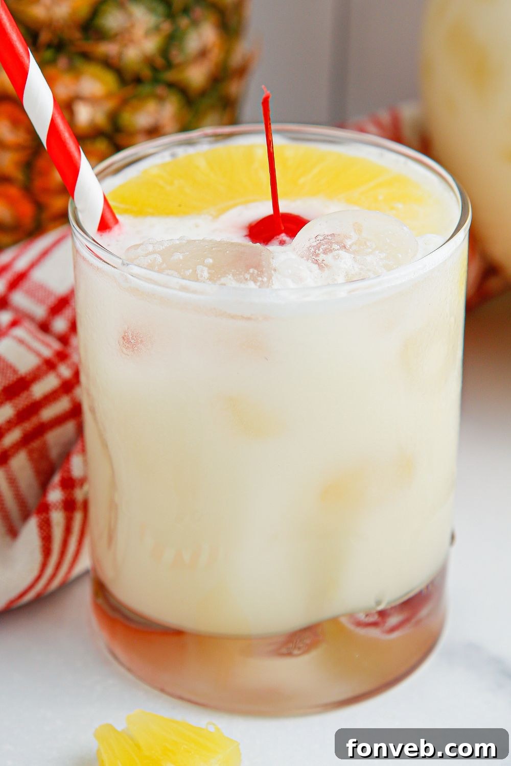 Island Escape Punch 10 A single glass of Piña Colada Punch, garnished with a red cherry and a small pineapple slice, with a red straw.