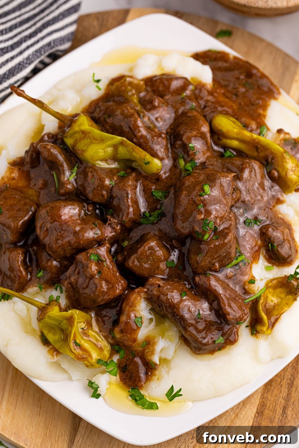 Tender Mississippi Crockpot Steak Bites 18 A modern square plate featuring Mississippi Steak Bites, garnished with a few whole pepperoncinis.