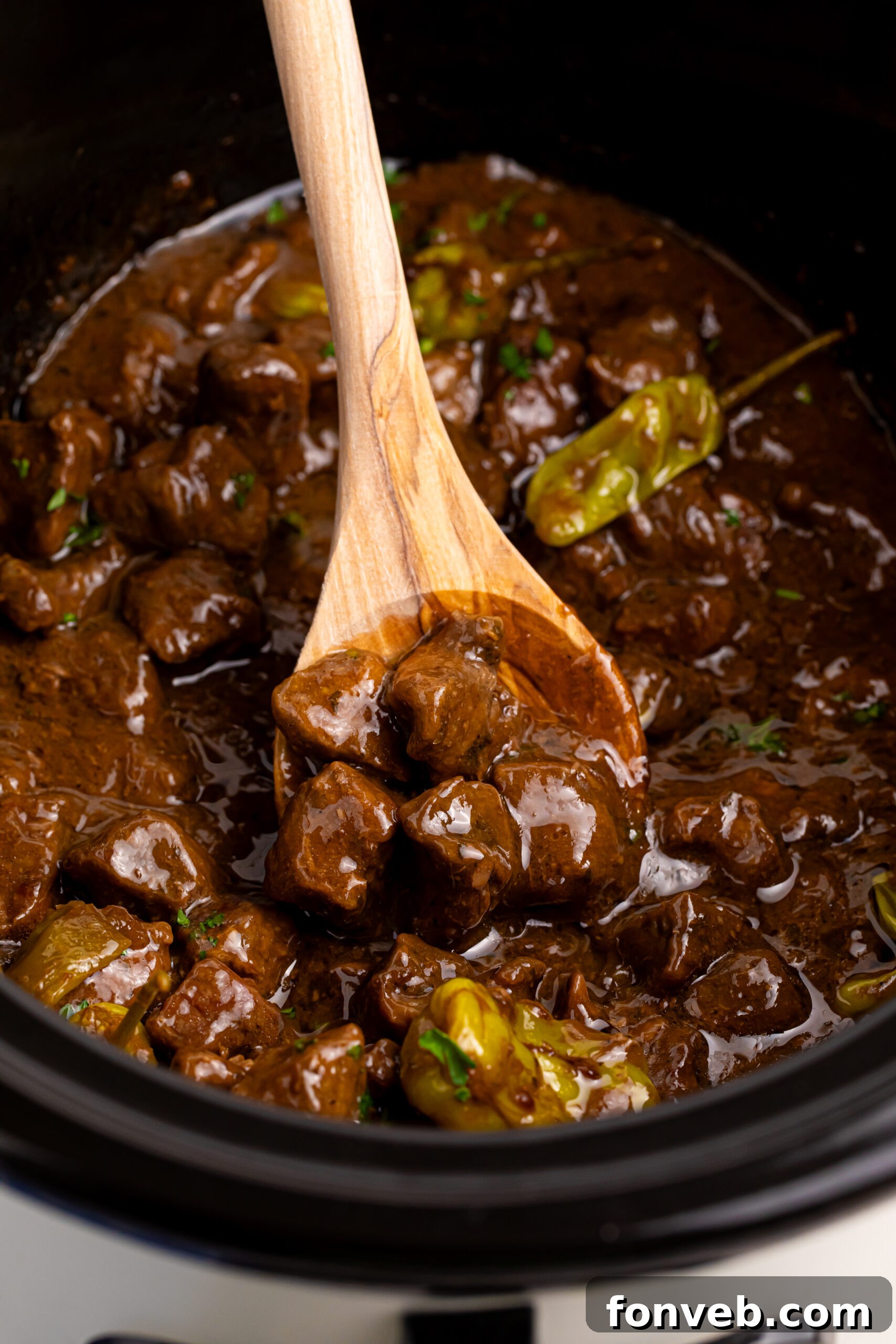Tender Mississippi Crockpot Steak Bites 20 Overhead view of Mississippi Steak Bites in a slow cooker with a wooden spoon, showcasing the tender meat and rich sauce.