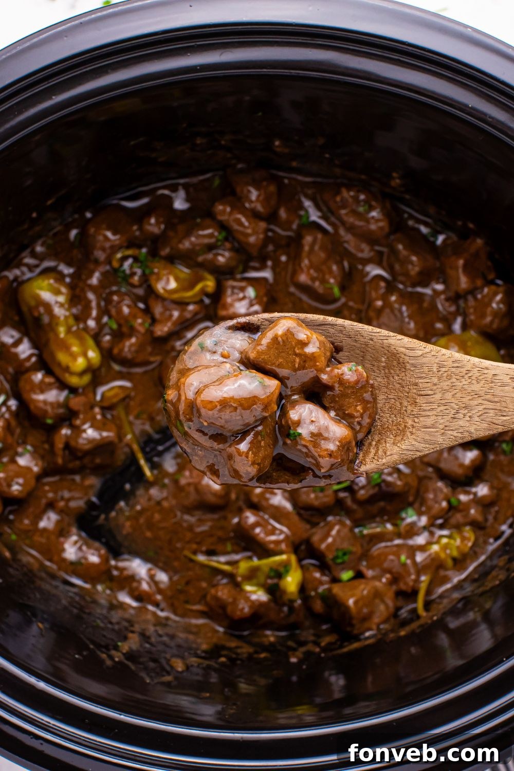 Tender Mississippi Crockpot Steak Bites 22 A wooden spoon holding up tender Mississippi Steak Bites over the slow cooker, ready to be served.