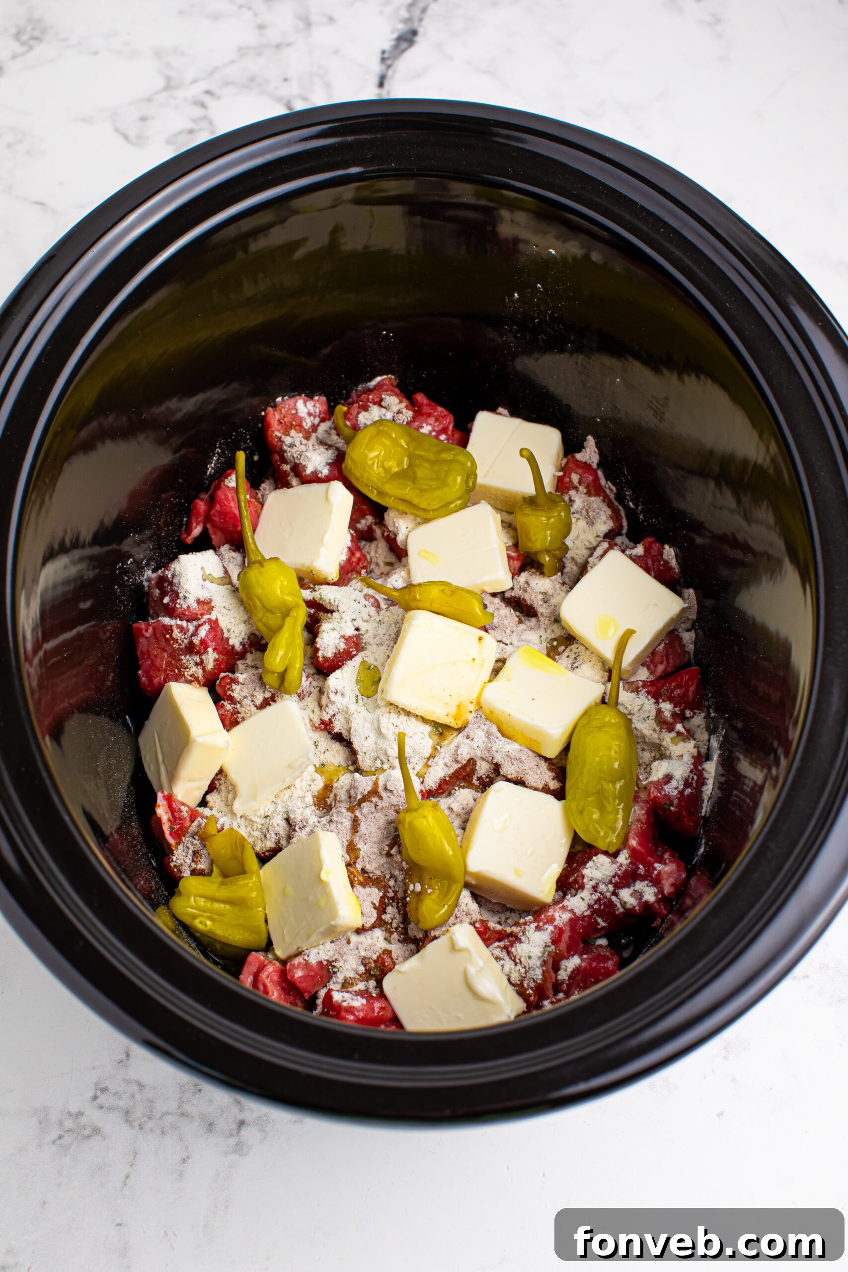 Tender Mississippi Crockpot Steak Bites 7 Diced sirloin steak in a slow cooker, topped with dry ranch and au jus seasoning, butter pats, and whole pepperoncini peppers.