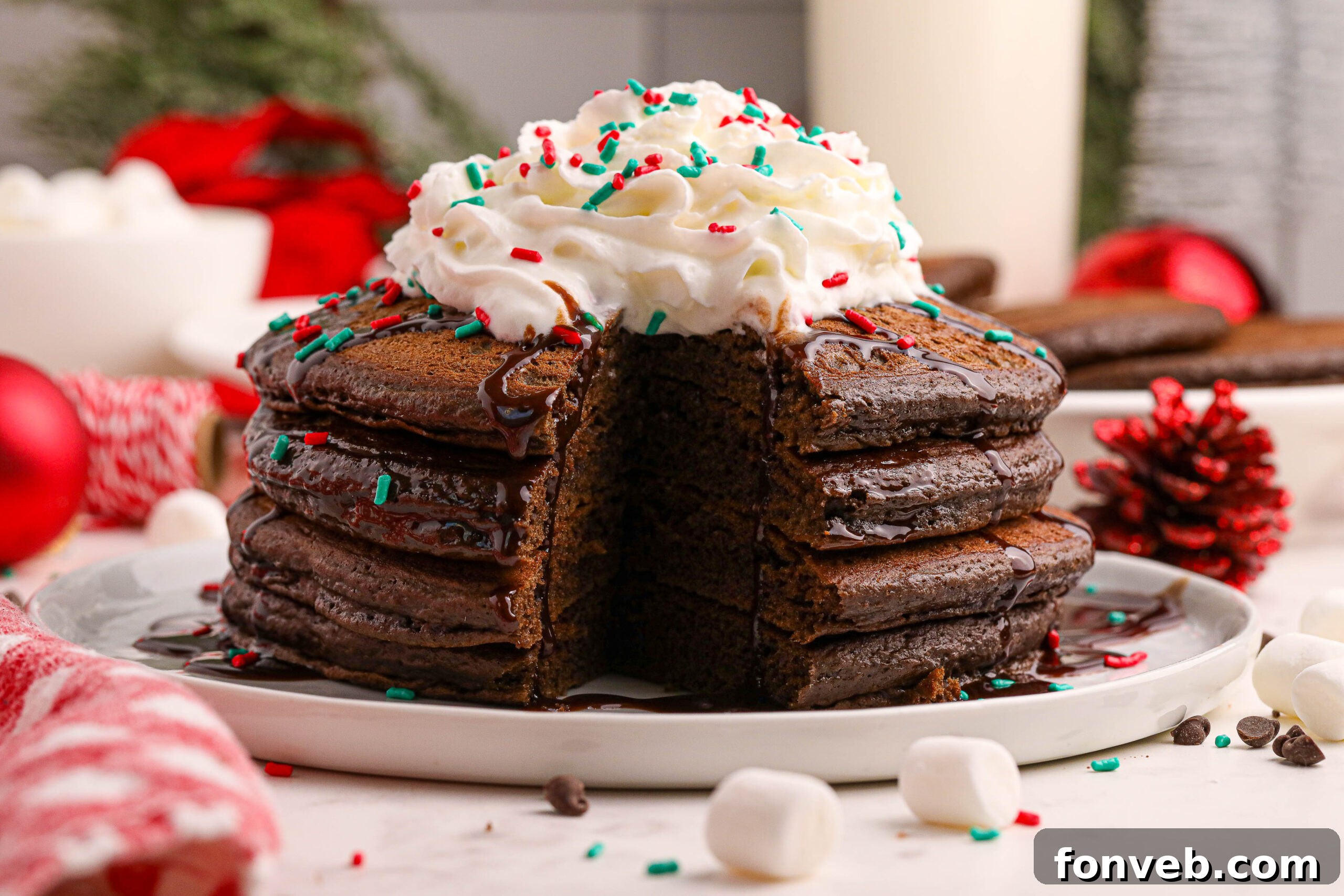 Decadent Hot Chocolate Pancakes 22 side view of Hot Chocolate Pancakes stacked on a plate topped with syrup and whipped cream and holiday sprinkles