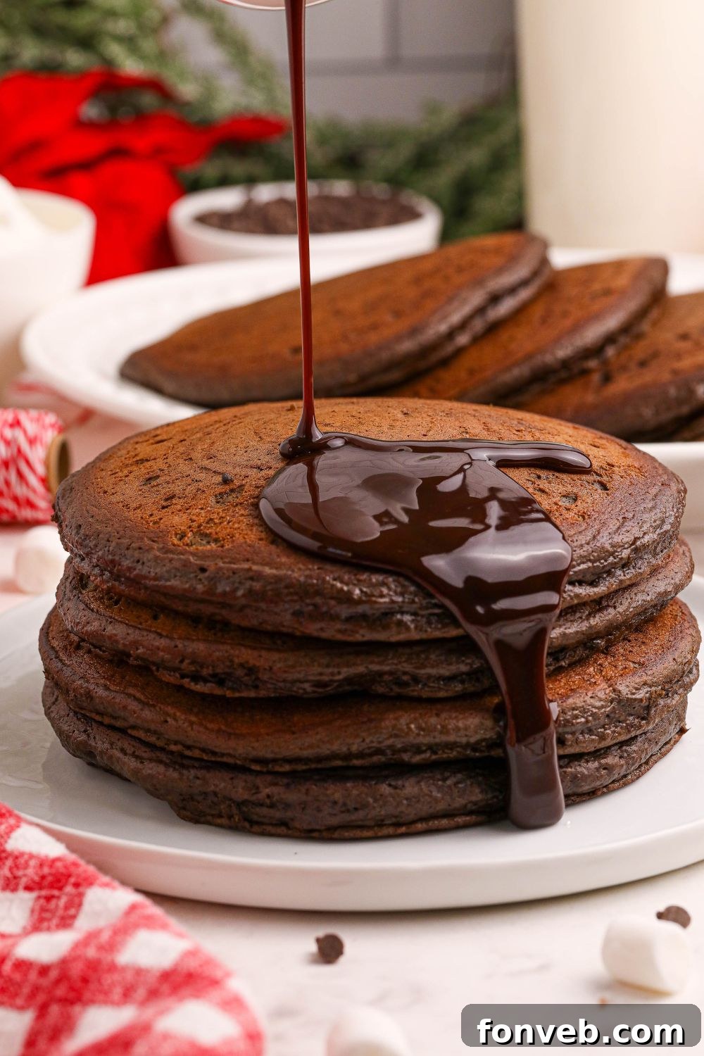 Decadent Hot Chocolate Pancakes 4 Hot Chocolate Pancakes stacked on plate with chocolate syrup pouring over the pancakes
