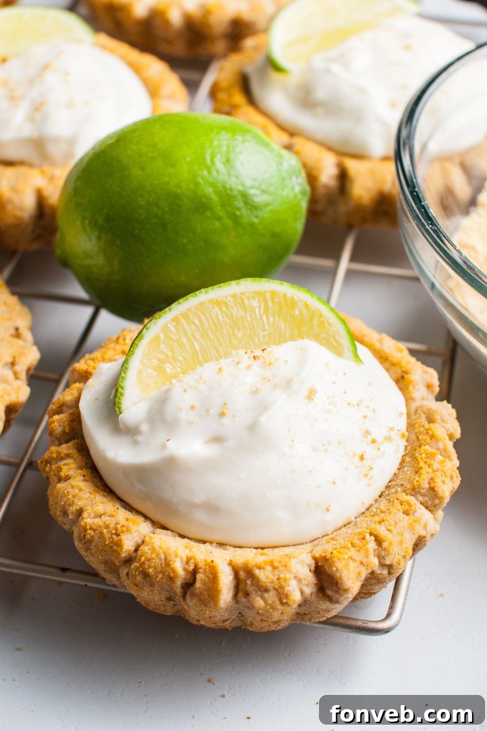 Tangy Key Lime Pie Cookies 17 Crumbl Key Lime Pie Cookies on a wire cooling rack with a lime wedge on each cookies and then a full lime on table