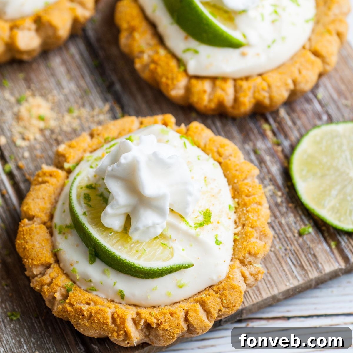 Tangy Key Lime Pie Cookies 3 Crumbl Key Lime Pie Cookies on table with lime wedges around and piles of graham cracker crumbs