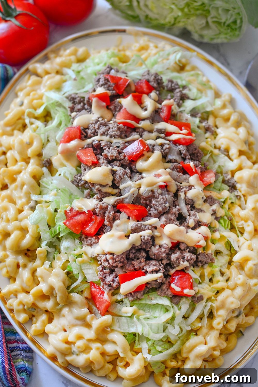 Big Mac Macaroni And Cheese on a platter on table with some tomatoes and lettuce in background 