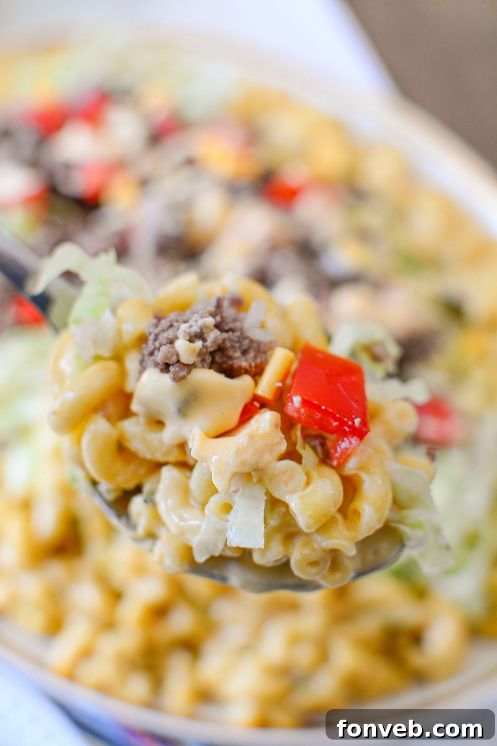 Big Mac Macaroni And Cheese on a spoon above the plate full of mixture that is sitting on table 