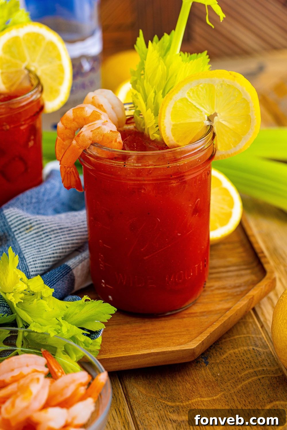 Bloody Mary on cutting board with shrimp and lemon and celery garnished and then food on table around drink 