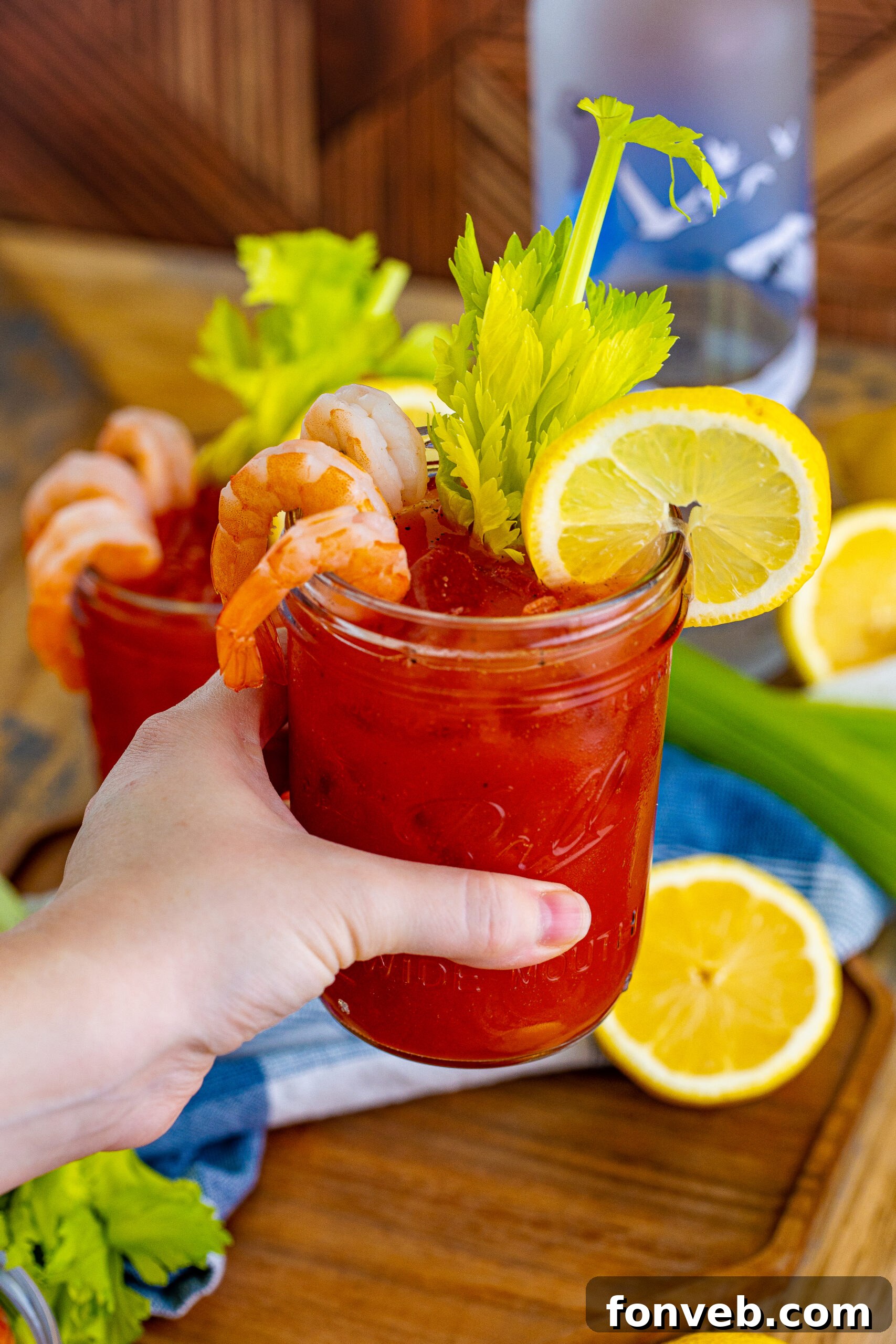 Bloody Mary in a clear mason jar glass with sliced lemon and shrimp being held up