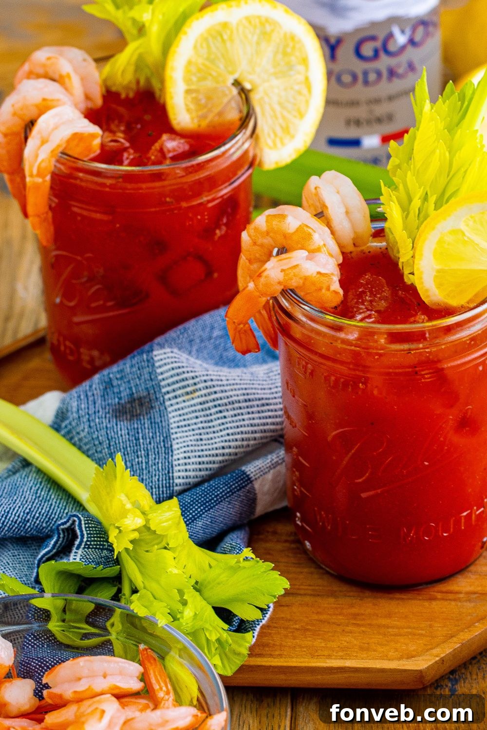 Bloody Mary sitting on table in glasses garnished with shirmp, lime, and celery 