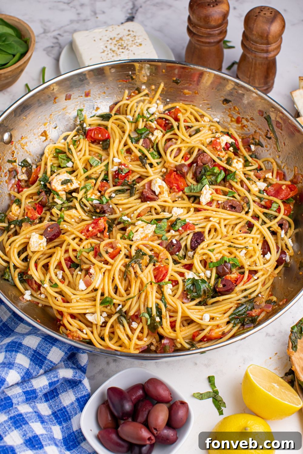 Greek Spaghetti in pan on table with olives and sliced lemon on the side, creating an inviting visual.