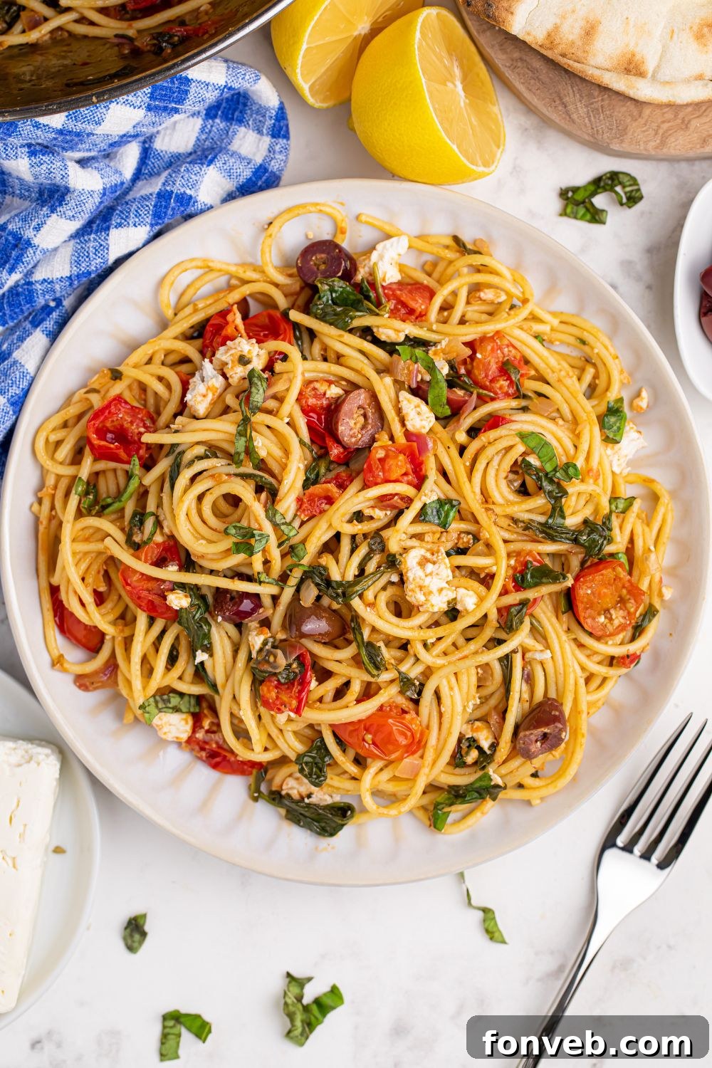 Greek Spaghetti on a plate with a towel and fork on table near the plate and lemon wedges around the plate, creating an inviting spread.