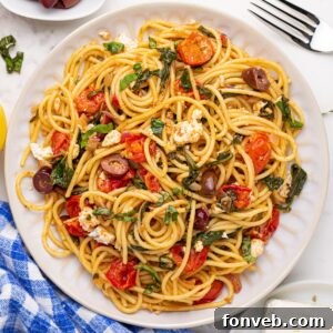 Greek Spaghetti on a plate with a fork to the side and a blue checkered towel