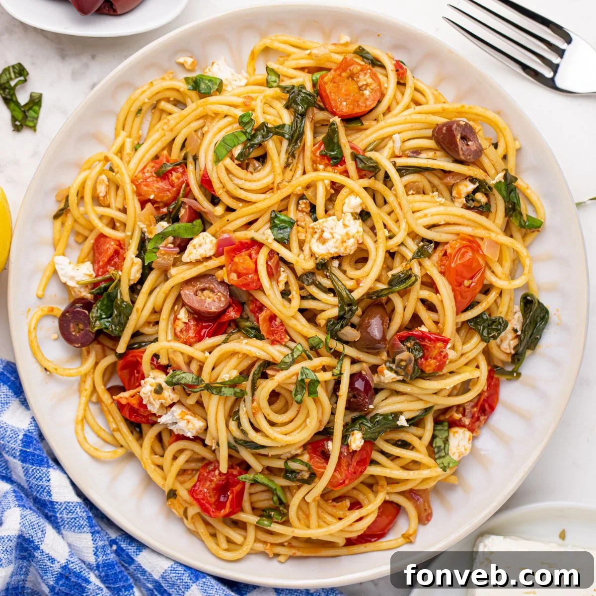Greek Spaghetti on a plate with a fork to the side and a blue checkered towel, setting a rustic dining scene.