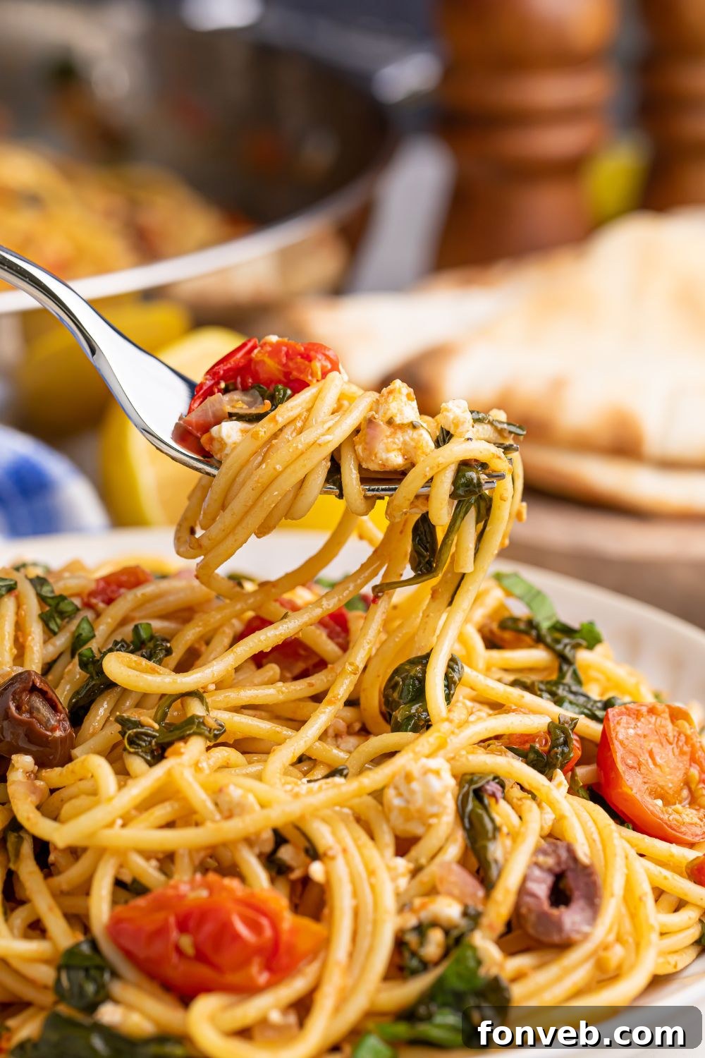 Greek Spaghetti on a plate with a fork above plate swirled with pasta and veggies, highlighting the fresh ingredients.