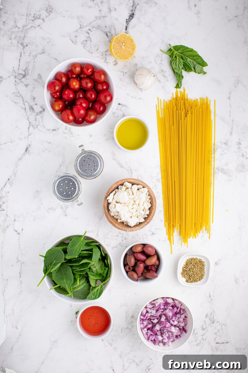 Greek Spaghetti ingredients laid out on a marble countertop, each in its own bowl, ready for preparation.