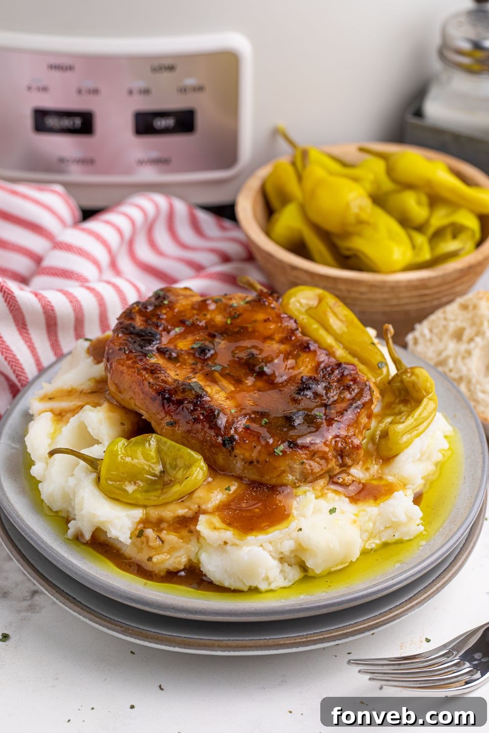 Crock Pot Mississippi Pork Chops on plate with a bowl of peppers in background and a crockpot 