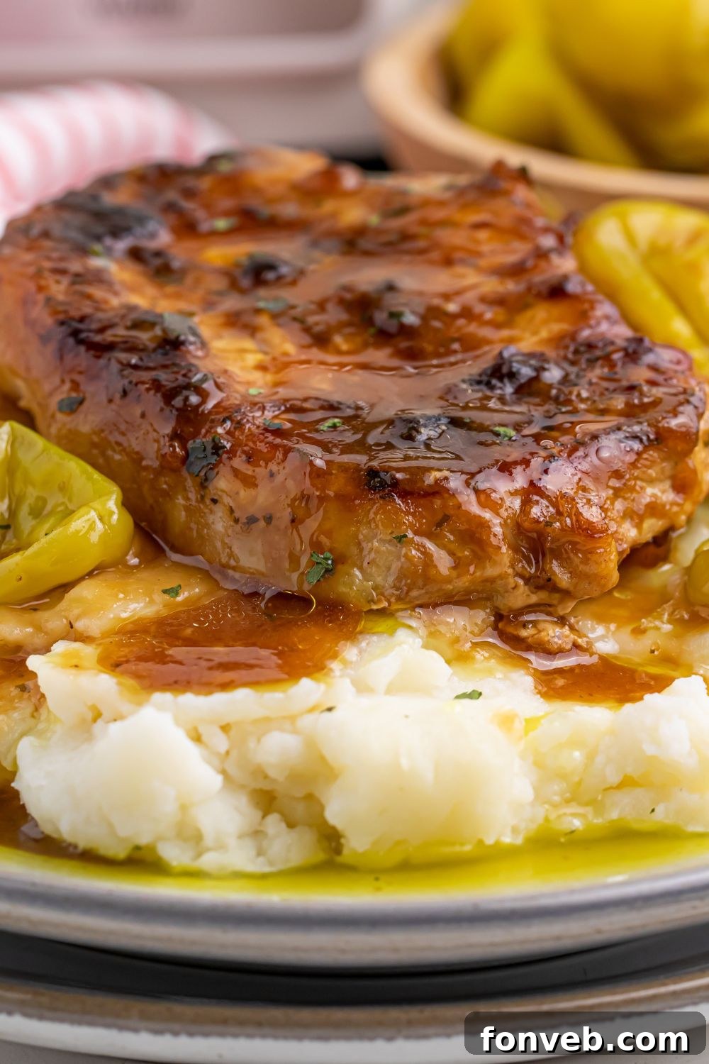 Crock Pot Mississippi Pork Chop on a plate with bed of mashed potatoes with peppers in a bowl on the side of plate 