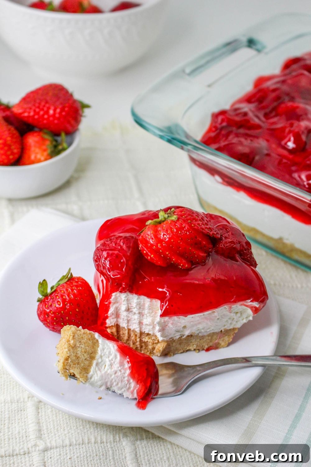 No Bake Strawberry Delight on plate with a bite and berry on plate and the pan beside it on table 