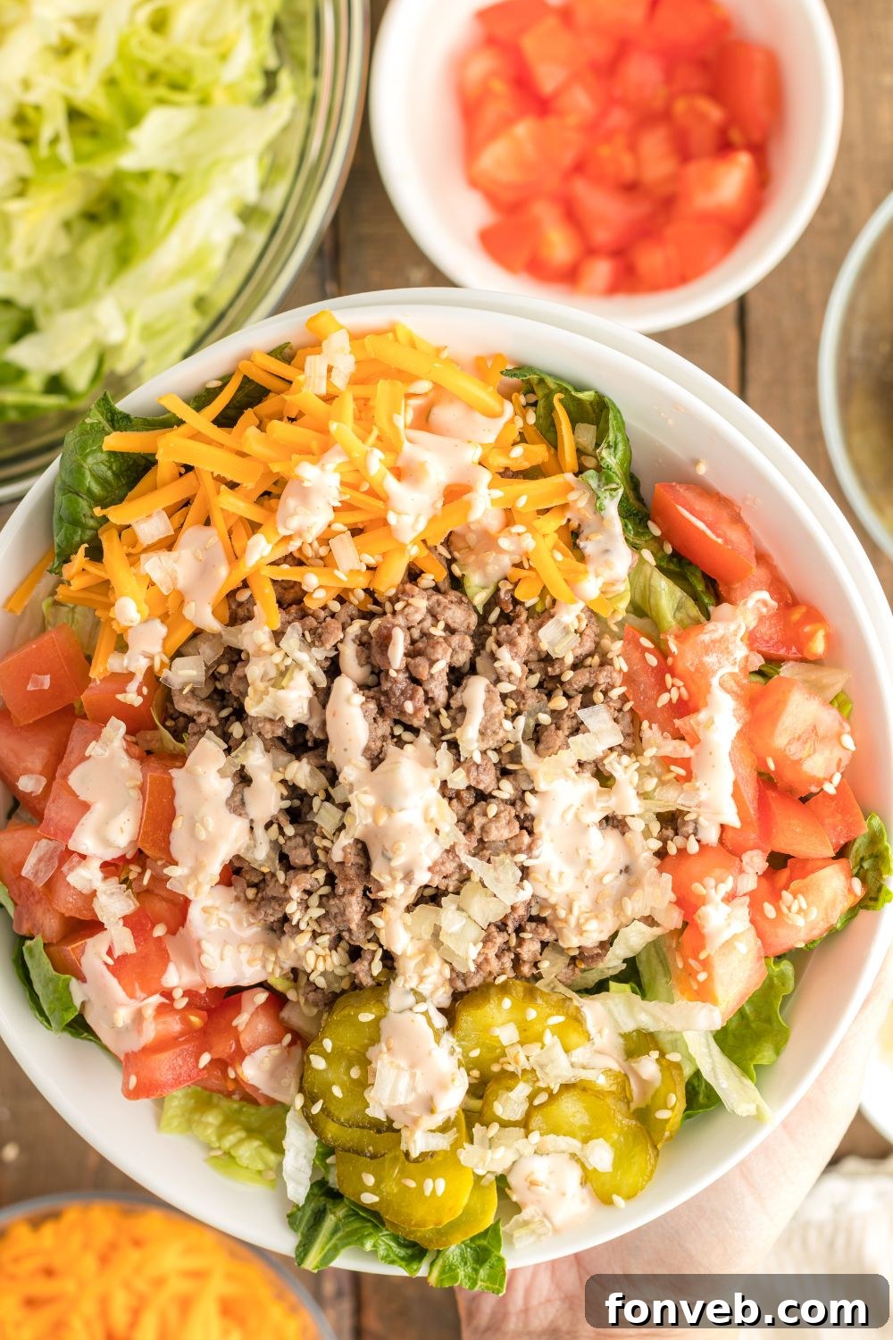 Big Mac Makeover Salad 2 Big Mac Salad in a bowl with an overhead view, surrounded by small bowls of individual ingredients like ground beef, pickles, cheese, and tomatoes.