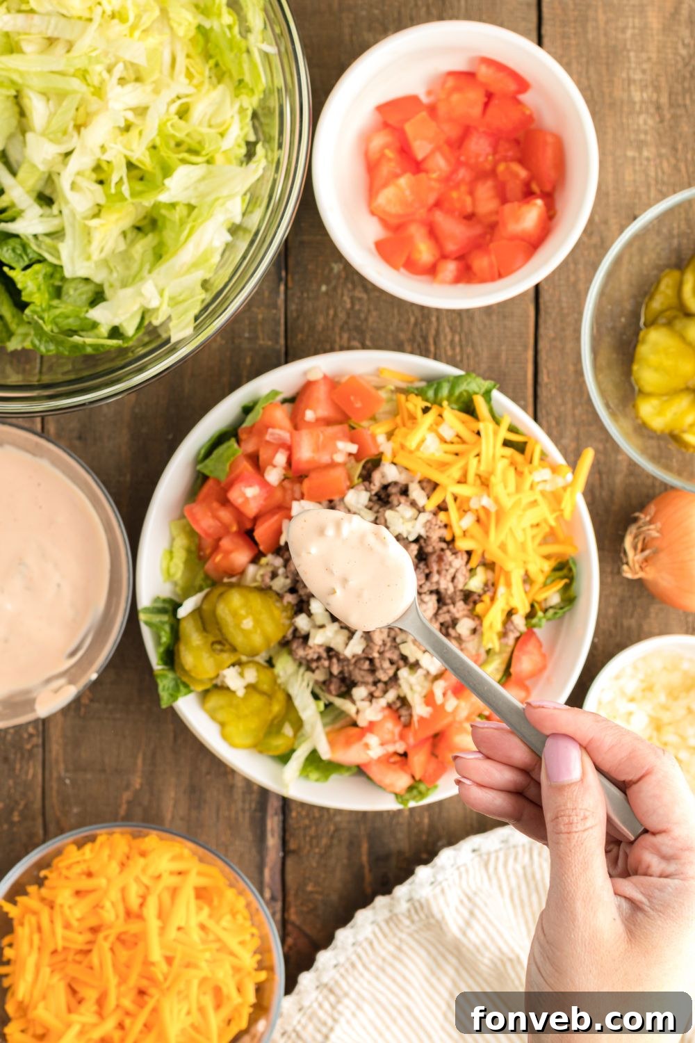 Big Mac Makeover Salad 11 Big Mac Salad dressing being delicately drizzled over the assembled salad using a small teaspoon, highlighting the rich texture of the sauce.