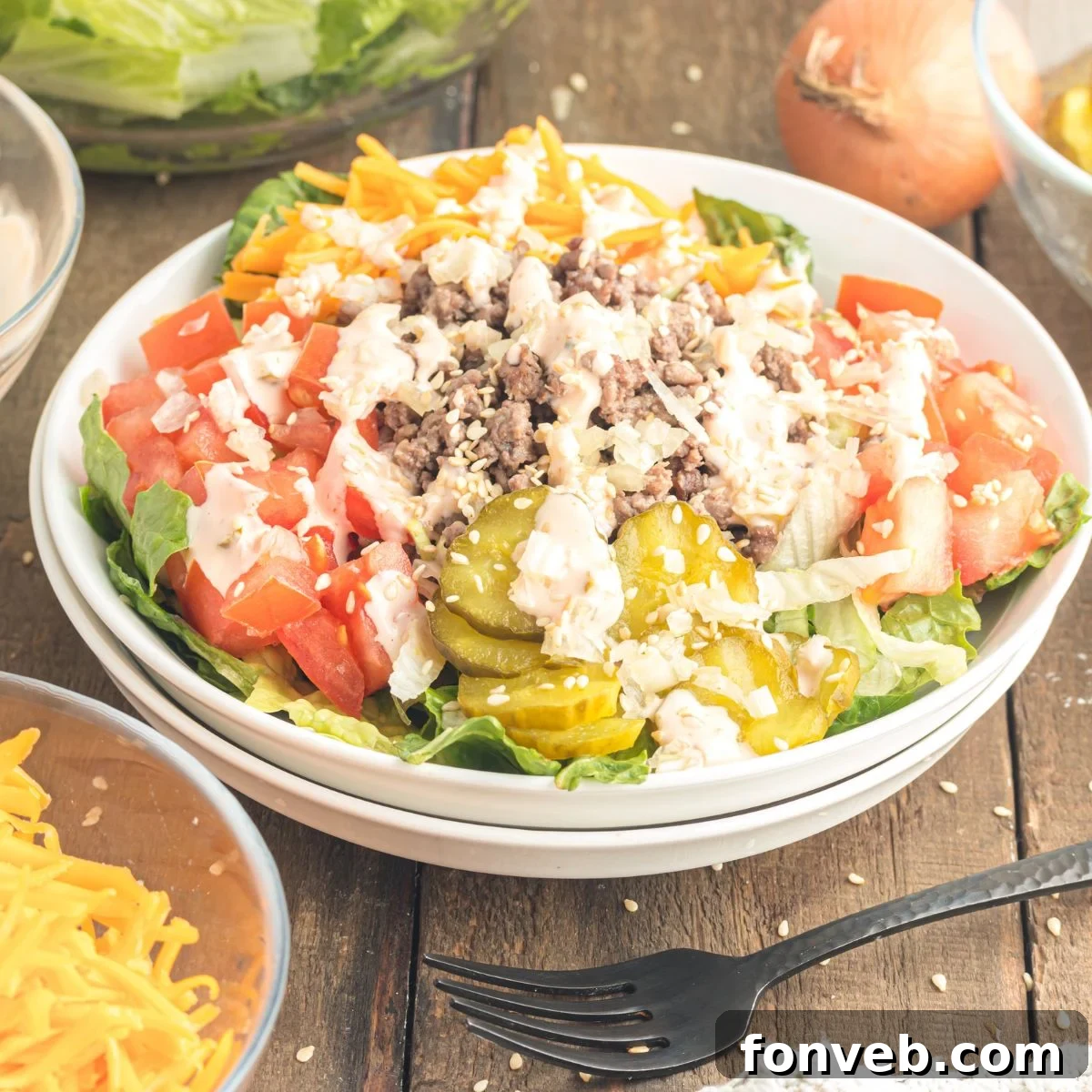 Big Mac Makeover Salad 3 Big Mac Salad served in a white bowl on a wooden table, with various fresh ingredients artfully arranged around it.