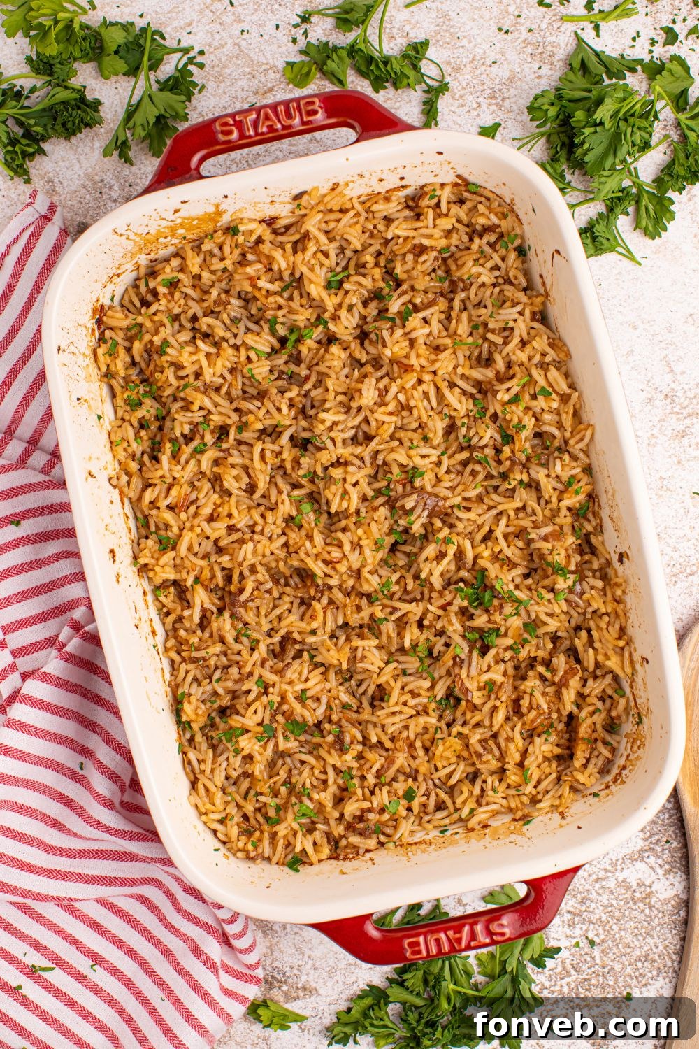 Stick of Butter Rice in casserole dish sitting on table with fresh parsley around it and a towel 