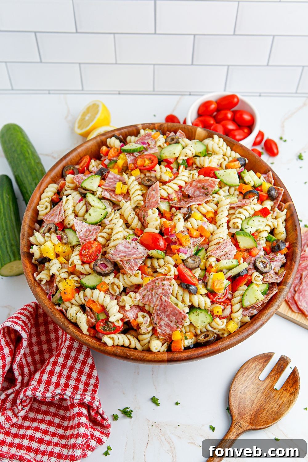 Summer Pasta Salad in a wooden bowl, surrounded by fresh, colorful vegetables on a table.