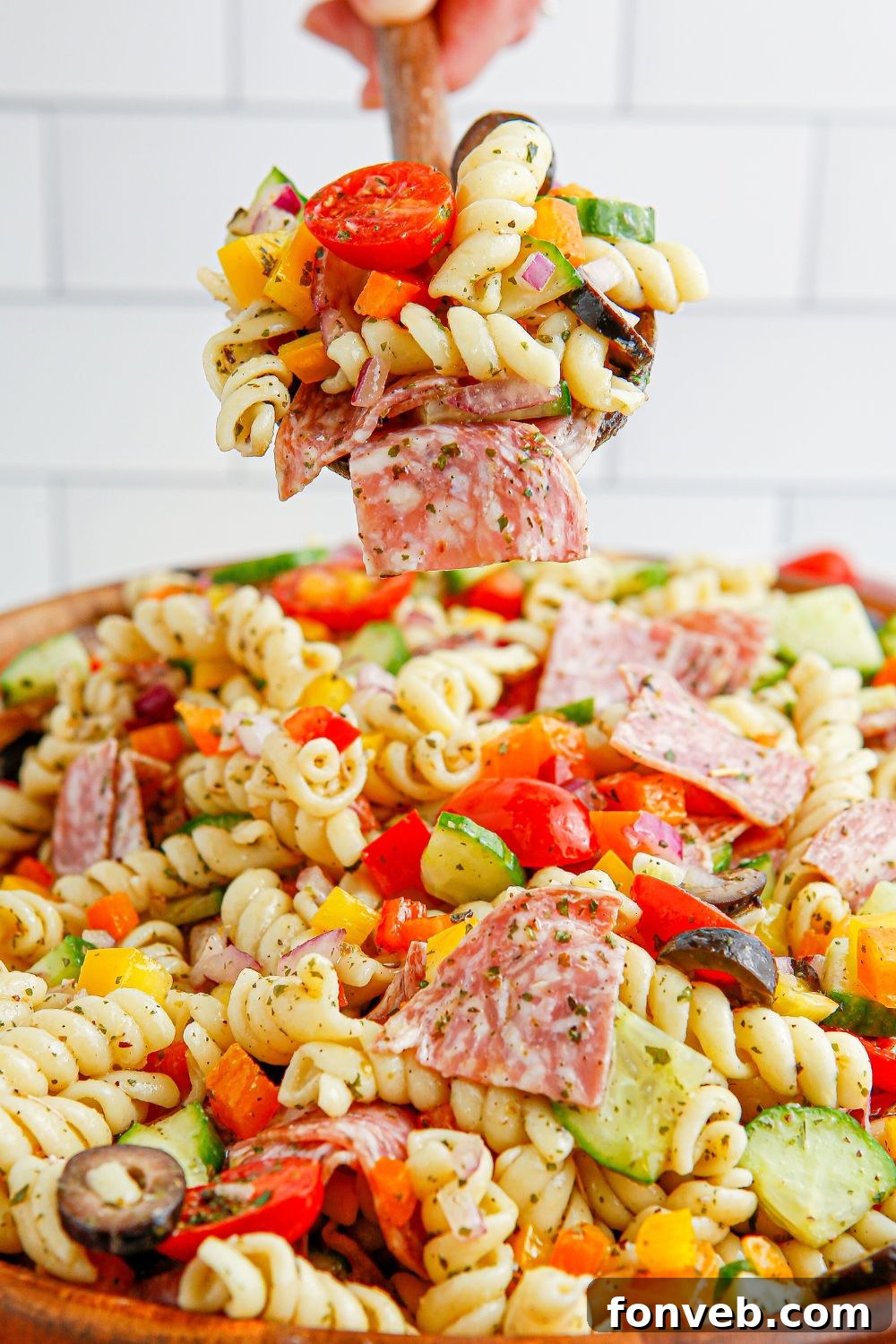 A spoon overflowing with Summer Pasta Salad, held above a bowl of the colorful dish.