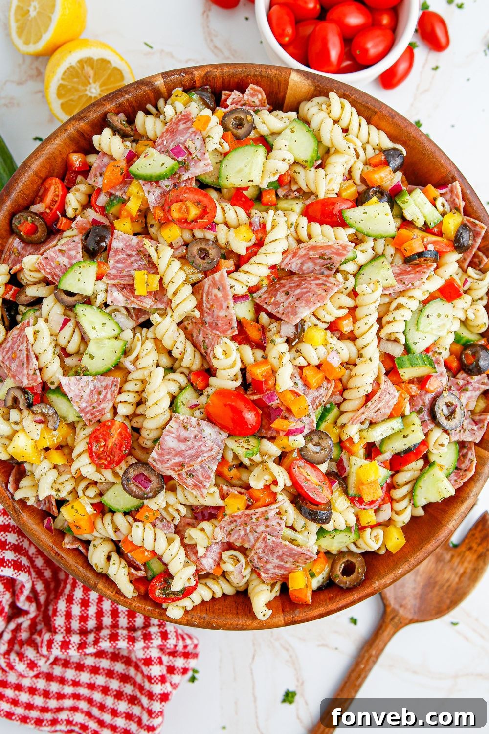 Summer Pasta Salad in a bowl, accompanied by a spoon and garnished with fresh tomatoes and lemon wedges on the side.