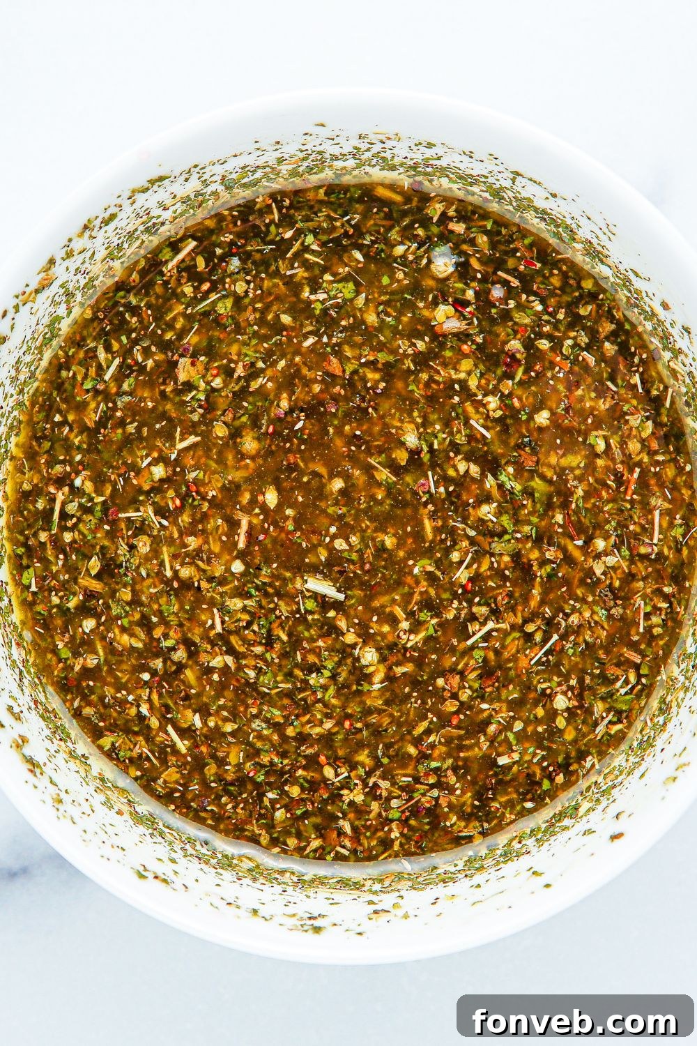 Close-up of the perfectly mixed homemade Italian dressing for Summer Pasta Salad in a white bowl.