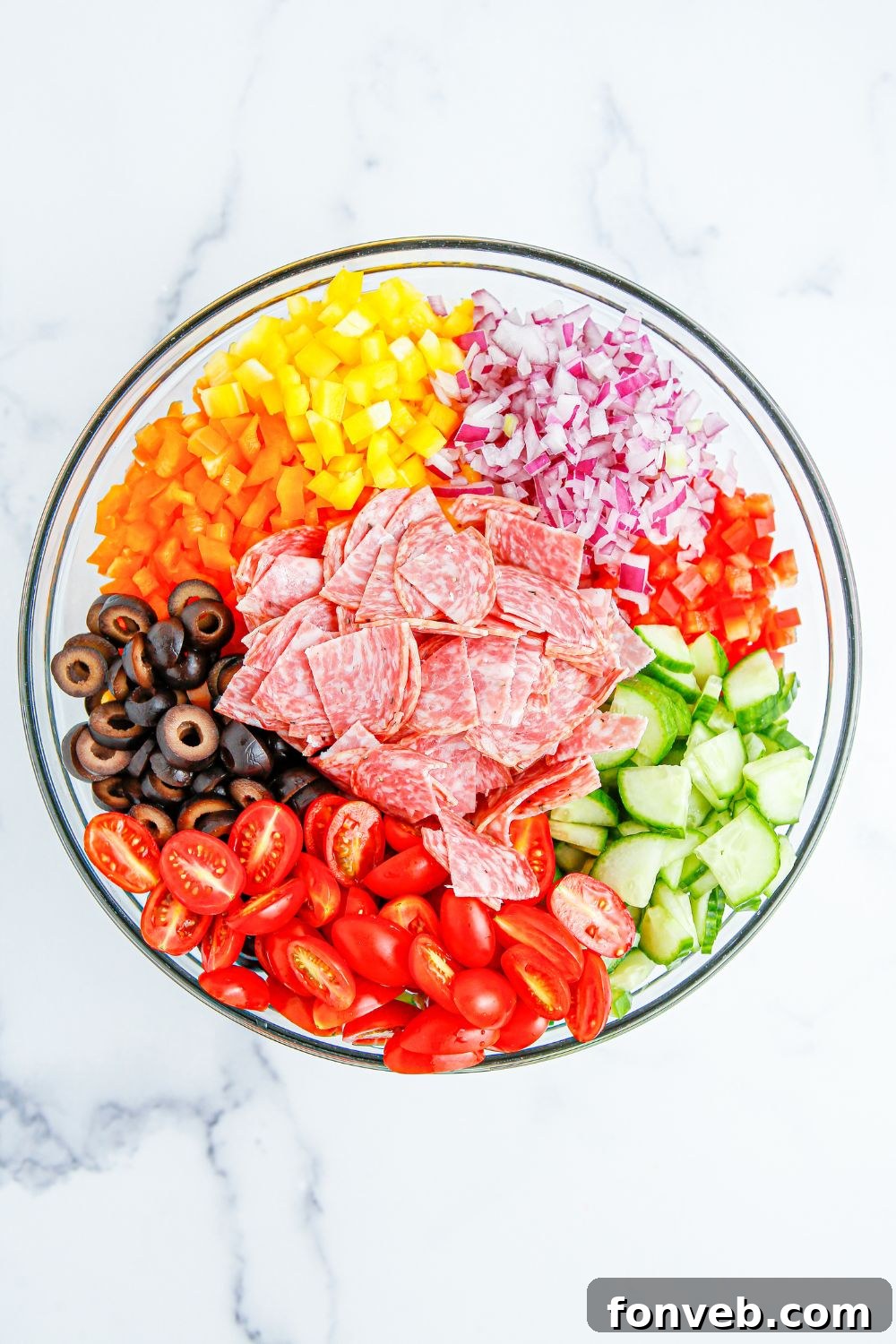 Various ingredients for Summer Pasta Salad, including diced vegetables and salami, arranged neatly in a large mixing bowl before tossing.