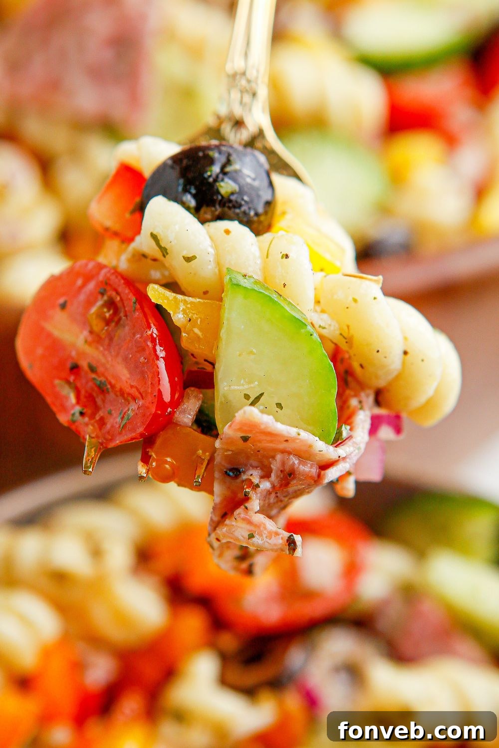 A fork lifting a portion of Summer Pasta Salad from a wooden bowl, showing the vibrant colors.