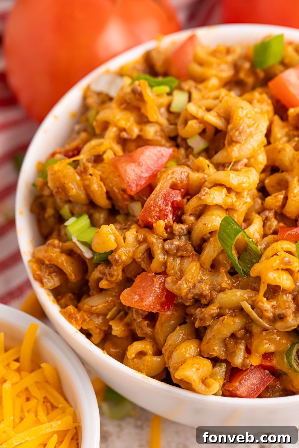 Taco Macaroni and Cheese in a bowl, generously topped with vibrant diced tomatoes and freshly chopped green onions.