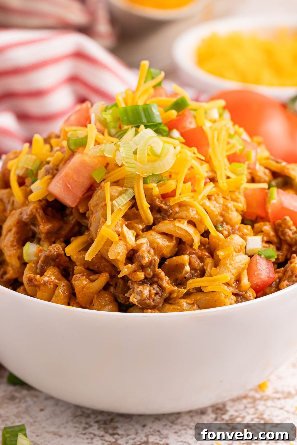 Taco Macaroni and Cheese in a white bowl, garnished with crisp shredded lettuce and diced ripe tomatoes for added freshness.