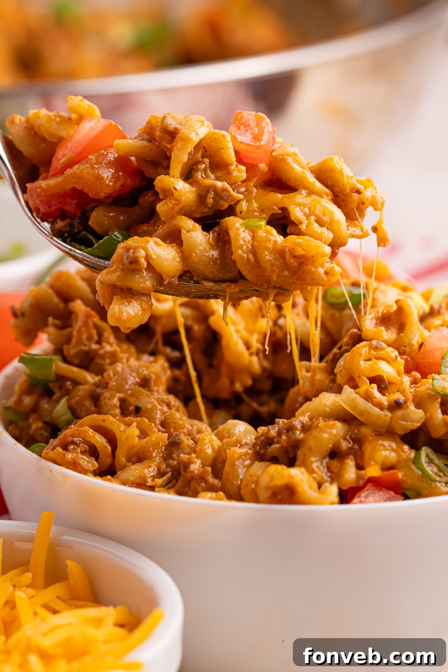 A white bowl filled with Taco Macaroni and Cheese, a fork ready to scoop a bite. The focus is on the rich, orange cheesy pasta.