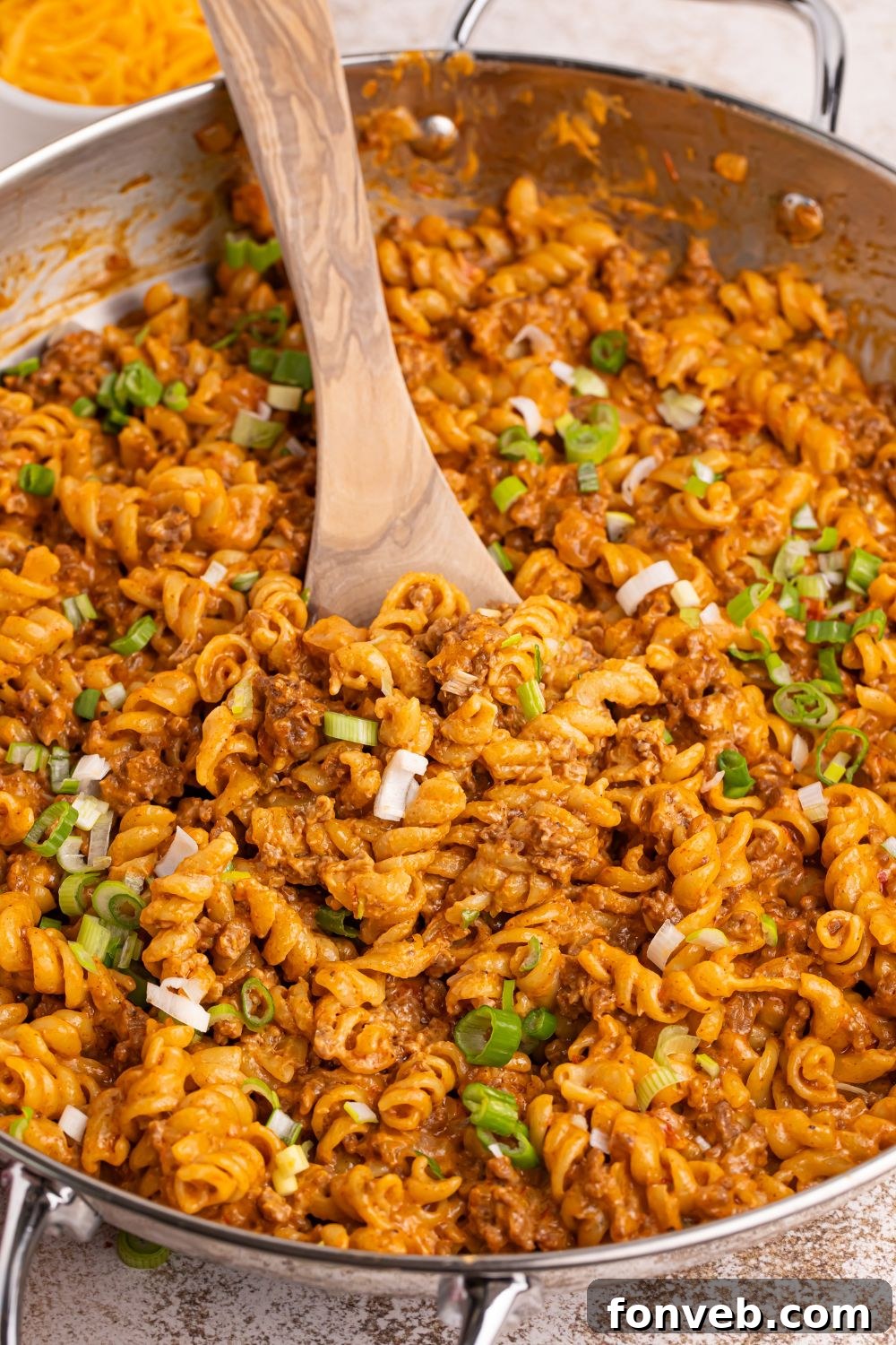 Taco Macaroni and Cheese in a large skillet, with a serving spoon poised to dish out. The surface is golden and inviting.
