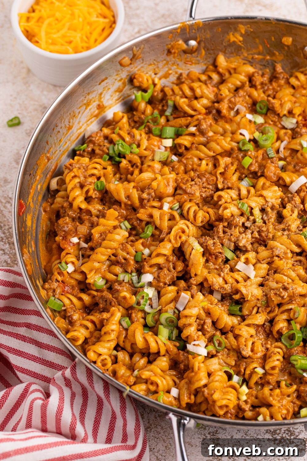 A skillet full of golden brown Taco Macaroni and Cheese, fresh from the stove, resting on a wooden board on a kitchen counter, ready to be served.