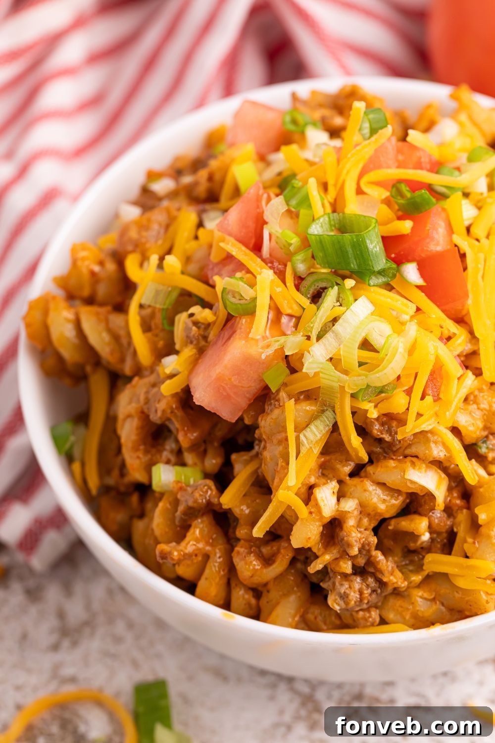 A serving of Taco Macaroni and Cheese in a bowl, topped with diced fresh tomatoes, a dollop of sour cream, and a sprinkle of vibrant green onions.