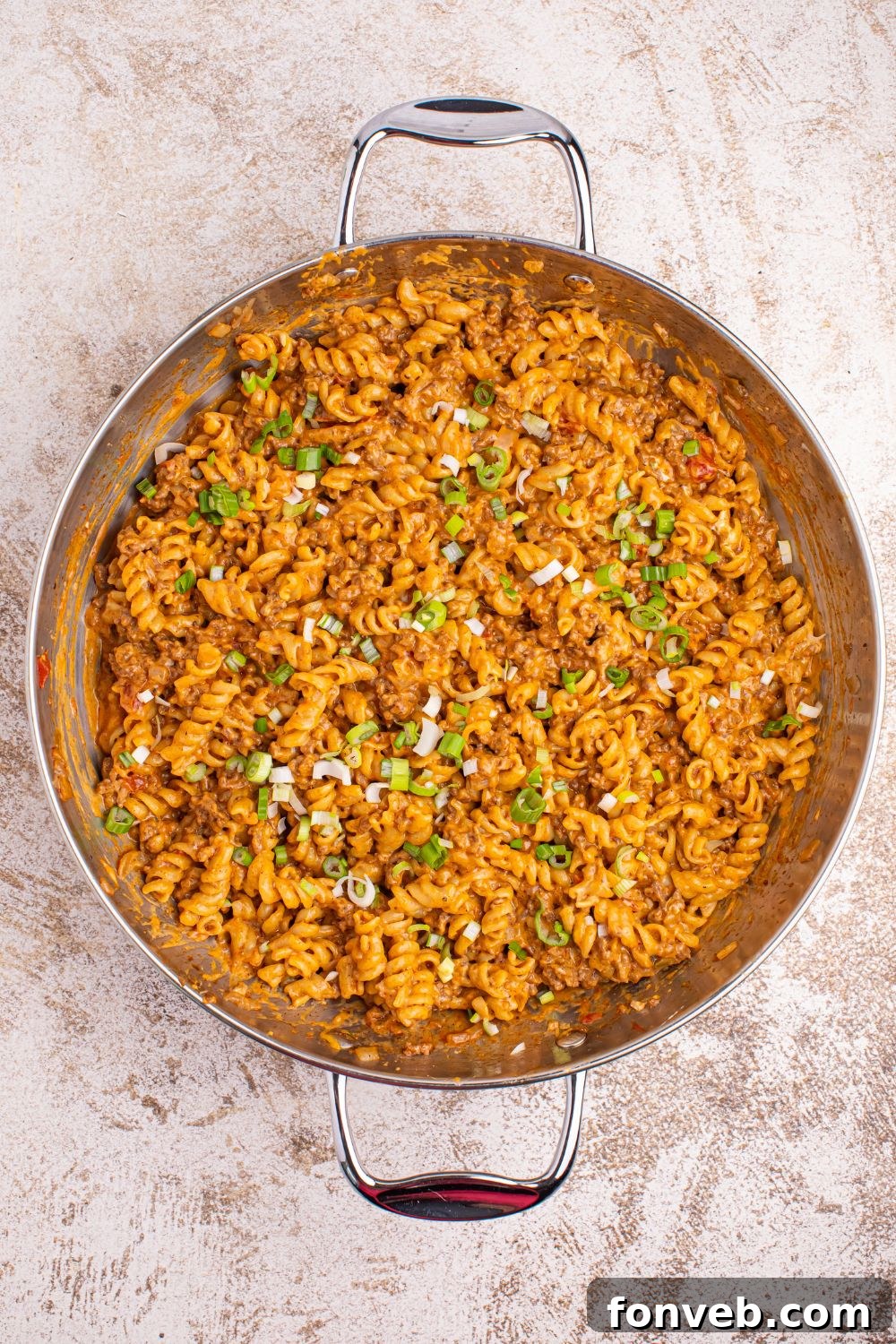 A close-up view of Taco Macaroni and Cheese in a pan, garnished with freshly chopped green onions and cilantro, ready for serving.