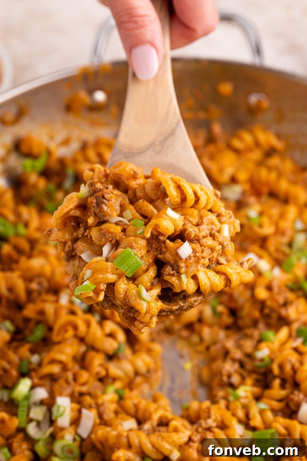 Taco Macaroni and Cheese simmering in a large skillet, with a wooden spoon stirring the creamy, cheesy mixture.