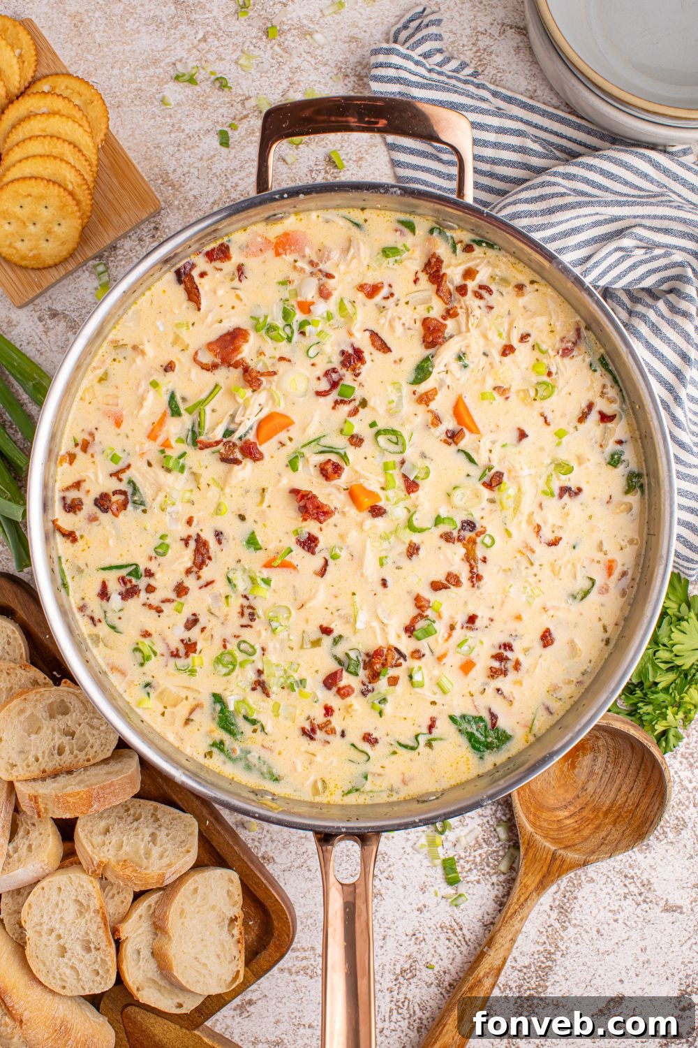 Overhead view of a rustic setup with a pot of Crack Chicken Soup, garnished, alongside fresh bread and herbs