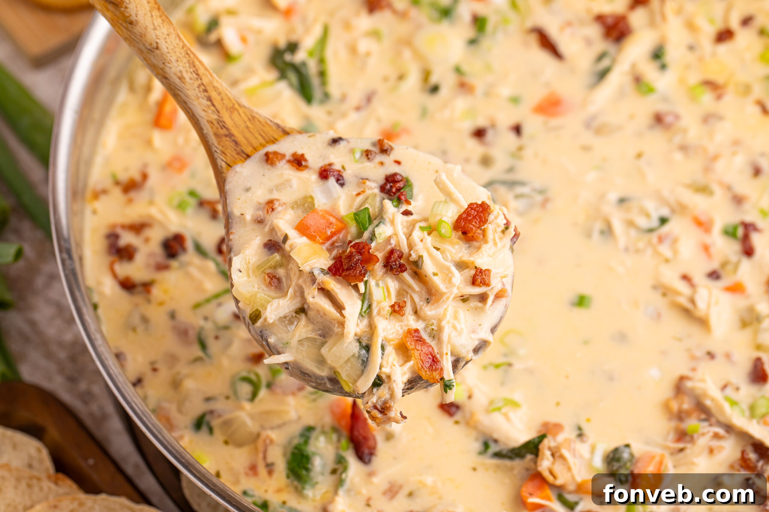 A wooden spoon holding a generous portion of creamy Crack Chicken Soup above the pot, showcasing its rich texture
