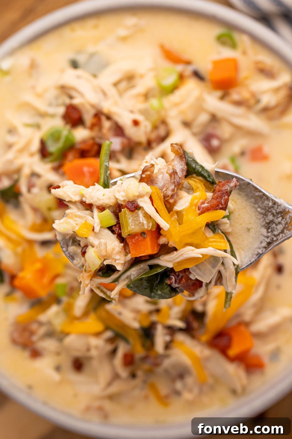A close-up shot of a spoon filled with creamy Crack Chicken Soup, held over a white serving bowl