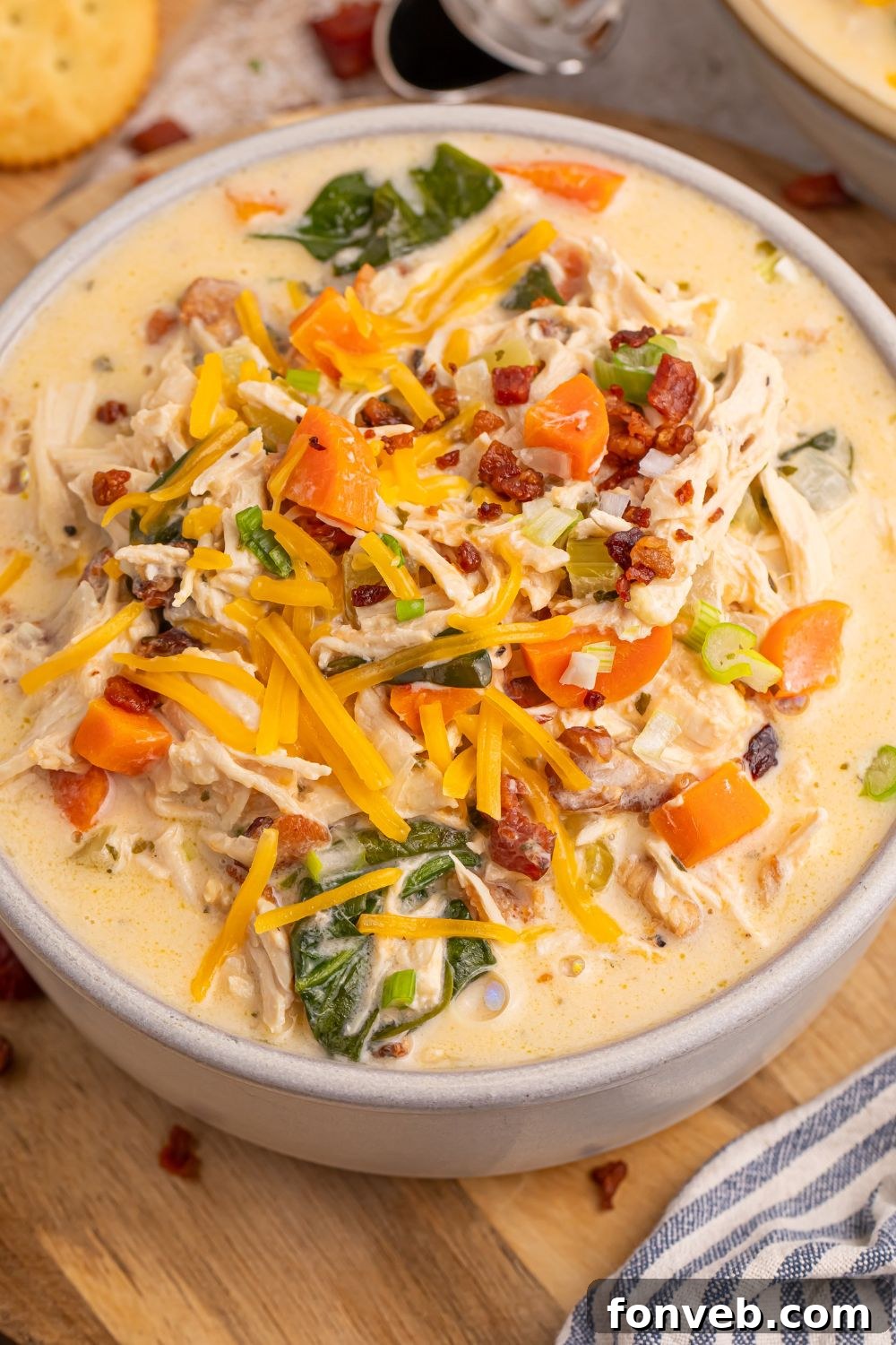 Close-up of a perfectly garnished bowl of Crack Chicken Soup on a table, topped with cheese and green onions