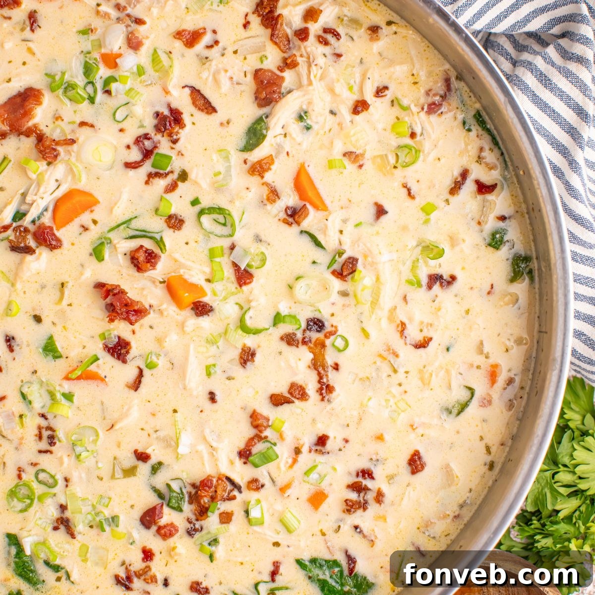 Close-up of creamy Crack Chicken Soup in a wide pan, garnished with herbs and bacon, resting on a towel