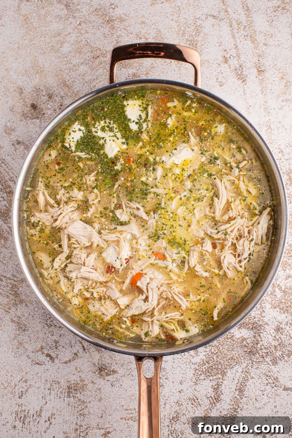 Close-up of creamy ingredients being stirred into the soup base in a large metal pan