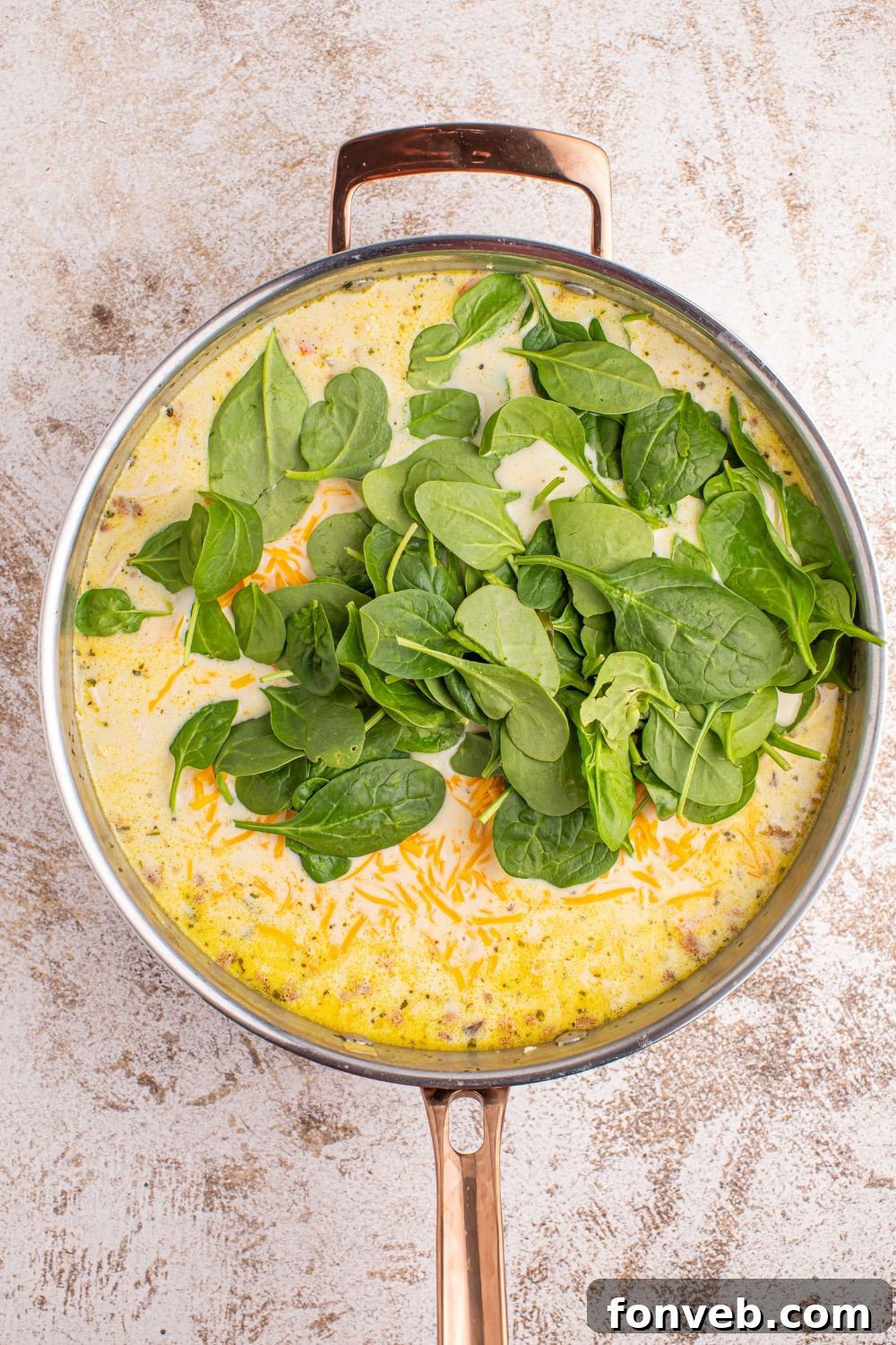 Fresh spinach being gently folded into the simmering Crack Chicken Soup in a large pot