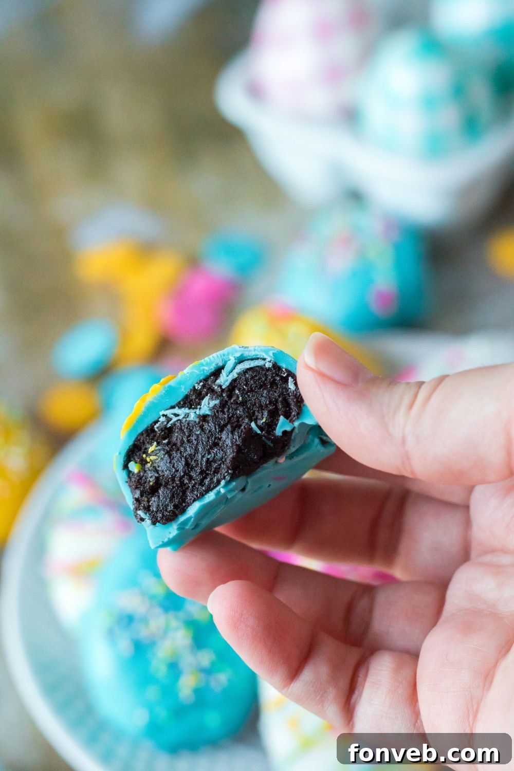 Festive Easter Egg Oreo Truffles 4 An Easter Egg Oreo Truffle held in hand, expertly bitten in half to reveal its rich, dark Oreo and cream cheese filling, contrasting beautifully with the colorful chocolate shell.